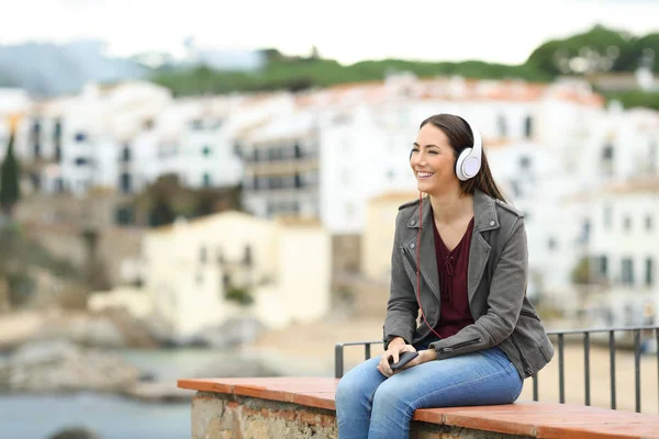 在海滨小镇度假时 快乐的女人带着耳机放松地听音乐 — 图库照片