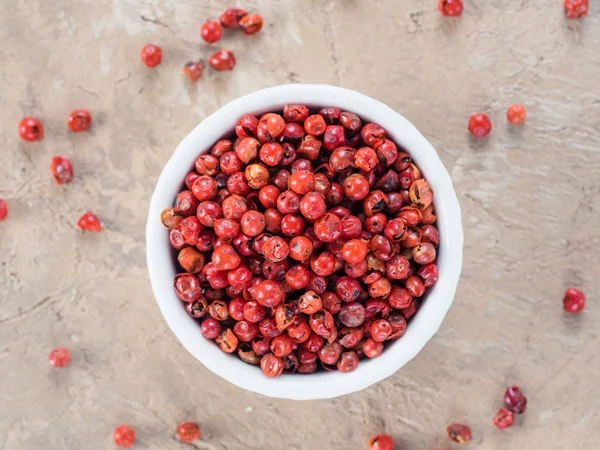 Pile with dried pink pepper berries on brown concrete background. Close up view of pink peppercorn. Top view or flat-lay.