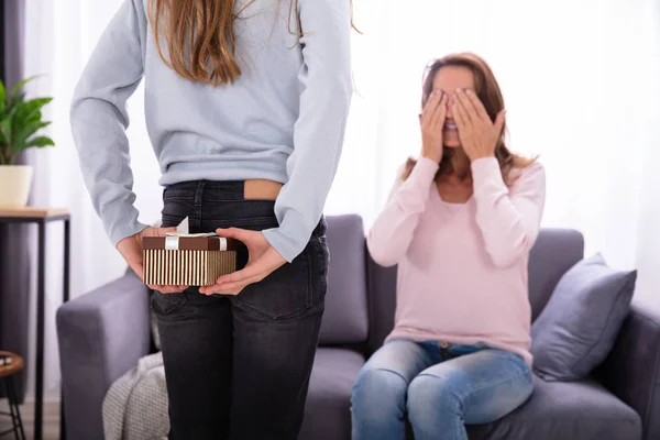 Menina Escondendo Presente Sua Mãe Sentada Sofá Cobrindo Olhos — Fotografia de Stock