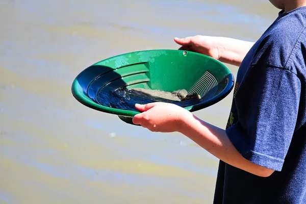 A childs hands holding a gold pan.