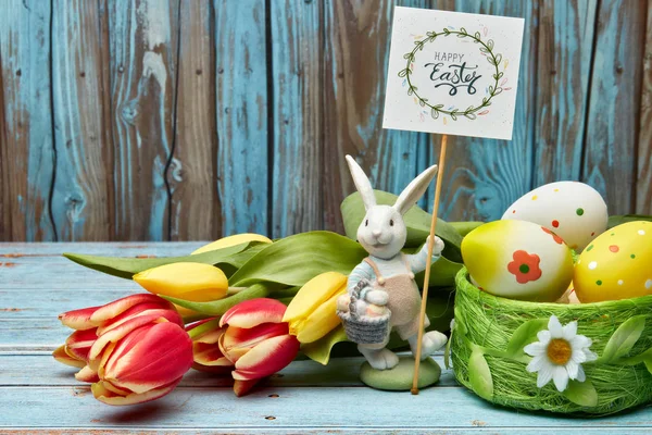 Colored easter eggs, easter rabbit and spring flowers on a wooden  background with copy space. Greeting card, Easter background