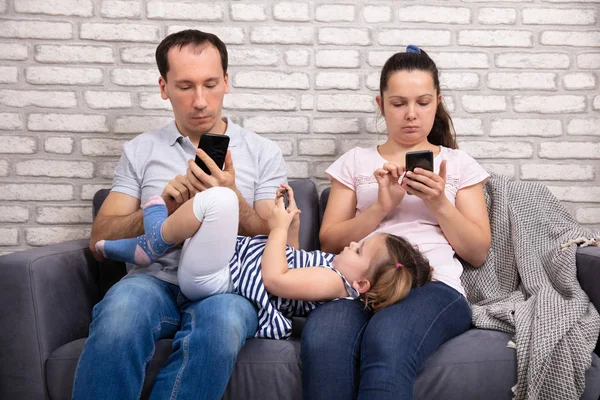 父母的正面看法与那里的女儿使用智能手机 而坐在沙发在家里 — 图库照片
