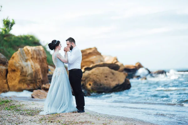 青いドレスを着た花嫁と同じカップルが海沿いを歩き — ストック写真