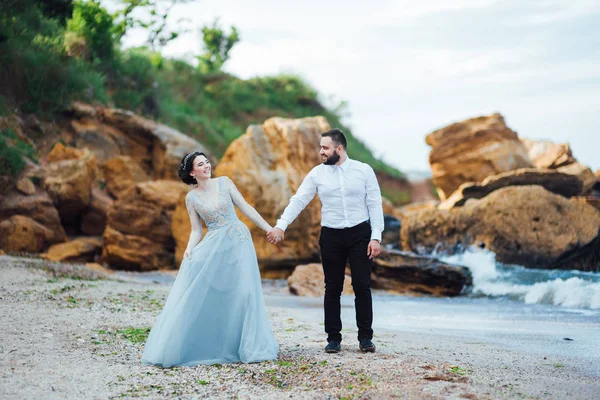 青いドレスを着た花嫁と同じカップルが海沿いを歩き — ストック写真
