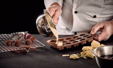 Chef or chocolatier pouring melted white chocolate into silicone molds from a saucepan in a close up on his hands clipart