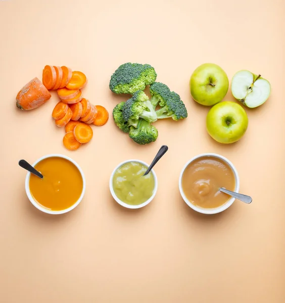 White bowls with healthy natural baby food on pastel background. Purees, made of fresh organic fruit and vegetables, flay lay, top view, concept. Food for kids made from carrot, broccoli, apples