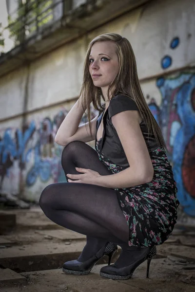 Young woman with leggings and mini dress post in front of graffiti paintings