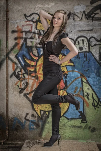 Young woman with leggings and mini dress post in front of graffiti paintings