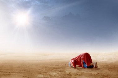 Rear view of asian muslim man praying in prostration position on desert with sun rays and dark sky background clipart