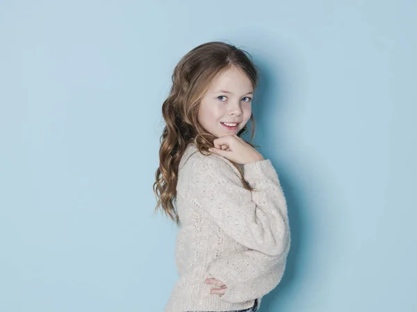 可愛くクールな9歳の女の子とともに茶色のウールセーターはスタジオで青の背景の前にポーズ — ストック写真
