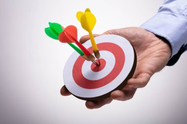 Close-up Of Human Hand Holding Colorful Darts On Target Against Background clipart