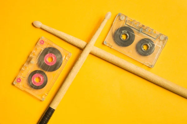 黄色の背景にドラムスティックとオーディオカセット — ストック写真