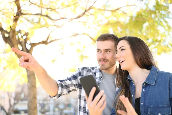 Casal Feliz Falando Apontando Para Longe Segurando Telefone Inteligente Parque — Fotografia de Stock