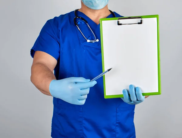医生穿着蓝色制服和无菌乳胶手套 手里拿着一个回形针和一支笔 显示手势 — 图库照片