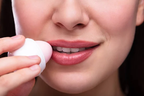 Smiling Young Woman Applying Balm On Her Lips