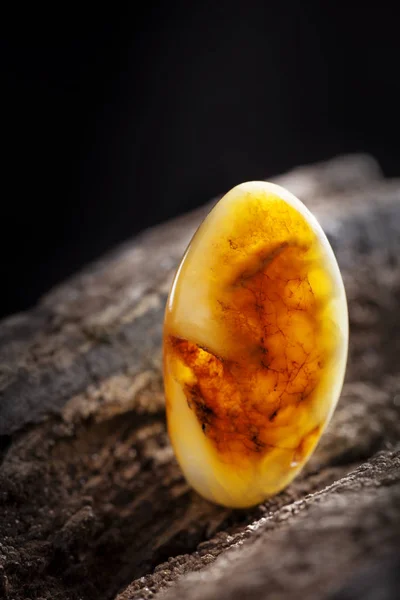 一块黄色半不透明的天然琥珀色 分类颜色的混蛋 里面有裂缝 有一个珠子的形状 放置在深色石头砸木纹理 — 图库照片