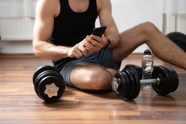 Άνθρωπος Κάθεται Ξύλινο Πάτωμα Στο Γυμναστήριο Χρησιμοποιώντας Smartphone — Φωτογραφία Αρχείου