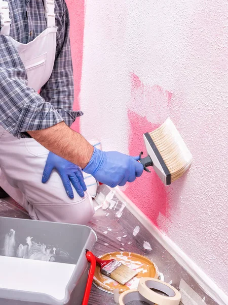 白いオーバーオールで白人の家の画家の労働者は ブラシが白い塗料でピンクの壁をペイントします 建設業 作業安全 — ストック写真