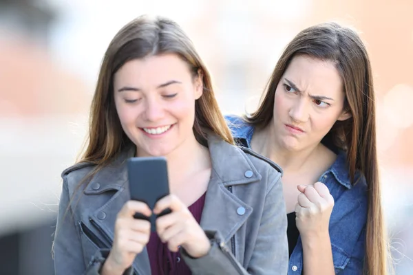 前视图肖像一个愤怒的女人窥探她的朋友在街上用手机 — 图库照片