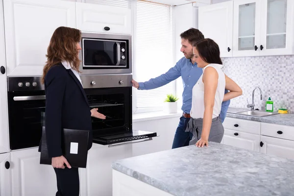 Agente Imobiliário Mostrando Forno Microondas Casa Para Jovem Casal — Fotografia de Stock