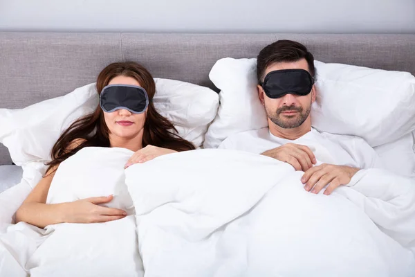 Young Couple Sleeping On Bed Using Eye Mask In Bedroom