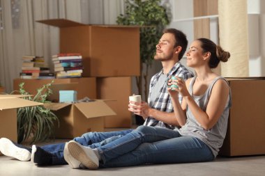 Happy couple moving home resting breathing fresh air sitting on the floor holding coffee cups clipart