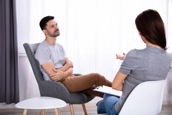 Jonge Man Zit Stoel Buurt Van Vrouwelijke Psycholoog Met Klembord — Stockfoto