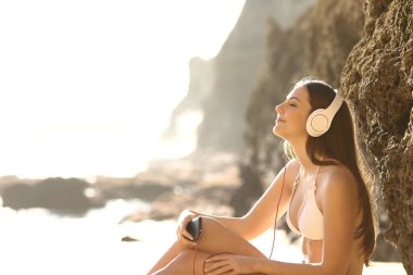 Side view portrait relaxed sunbather listening to music with smart phone and headphones on the beach clipart