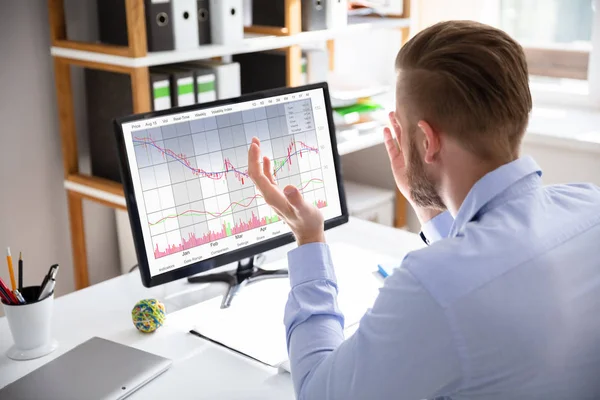 Despairing businessman faced with financial losses sitting at his desk consulting graphs on monitors