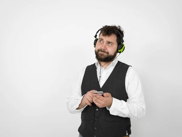 cool man with black beard is posing with headphones and smartphone in front of white background and is happy