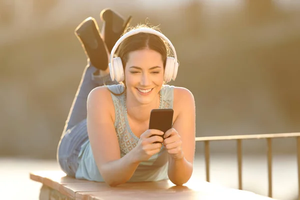 一个快乐的女孩听音乐浏览智能手机内容的全身肖像 — 图库照片