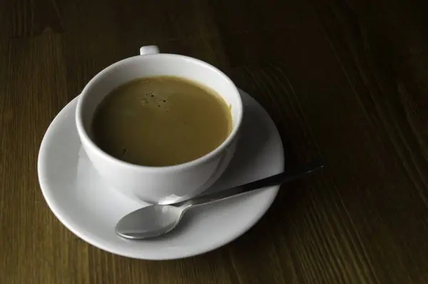 放在棕色桌子上的一杯咖啡和一把勺子 — 图库照片