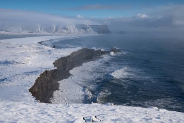 Panoramic image of the coastal landscape of Cape Dyrholaey on a winter day with snow-covered coastline, Iceland clipart