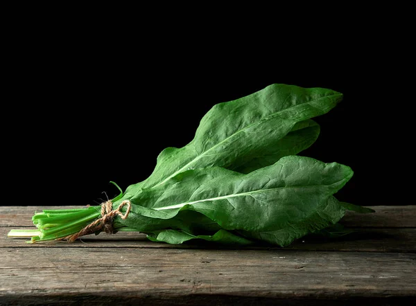 fresh green leaves of sorrel are bound in a bunch on a wooden table, black background