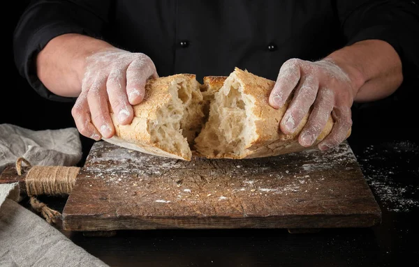Piekarz Czarnym Mundurze Złamał Pół Całego Pieczonego Bochenka Chleba Mąki — Zdjęcie stockowe