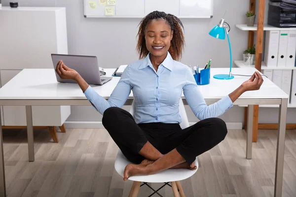 Relaxed Young Businesswoman Meditating In Lotus Position On Desk
