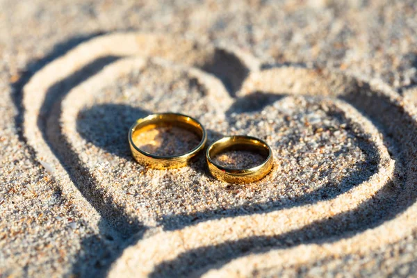 ビーチの砂の上のハートの形の中の黄金の結婚指輪のオーバーヘッドビュー — ストック写真