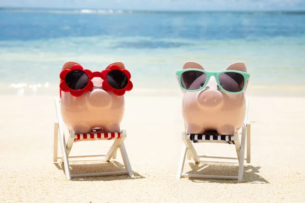 两个粉红色的小猪银行与不同类型的太阳镜在海滩的甲板椅的特写 — 图库照片