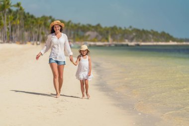Young mother and little daughter walking on the beach in Dominican Republic clipart