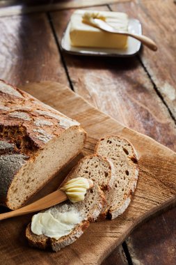 Sliced crusty loaf of fresh rye bread with butter and a butter knife or spreader on an old rustic wooden board on a table with copy space clipart