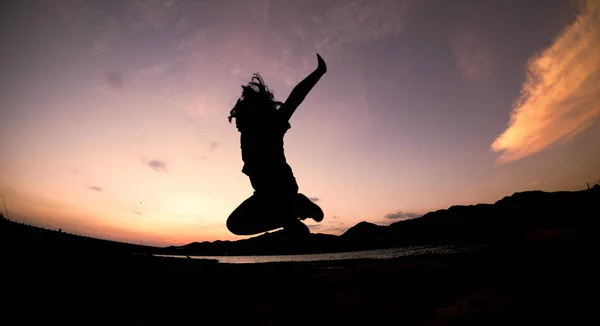 シルエット 夕方にオレンジ色の空にジャンプ幸せなジャンプシャドウガール — ストック写真