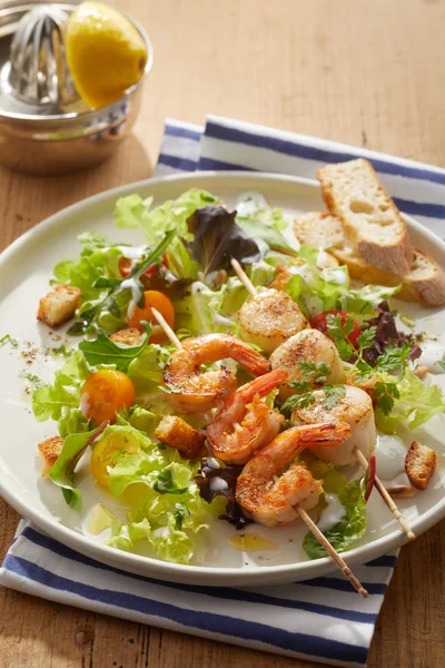 Grilled spicy scampi or baby lobster tails with scampi served on wooden skewers on a bed of leafy salad greens with crunchy fried croutons and sliced baguette