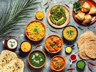 Indian cuisine dishes: tikka masala, dal, paneer, samosa, chapati, chutney, spices. Indian food on gray background. Assortment indian meal top view or flat lay. clipart
