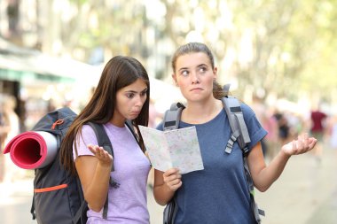 Two lost backpackers trying to find location consulting a paper guide in the street clipart