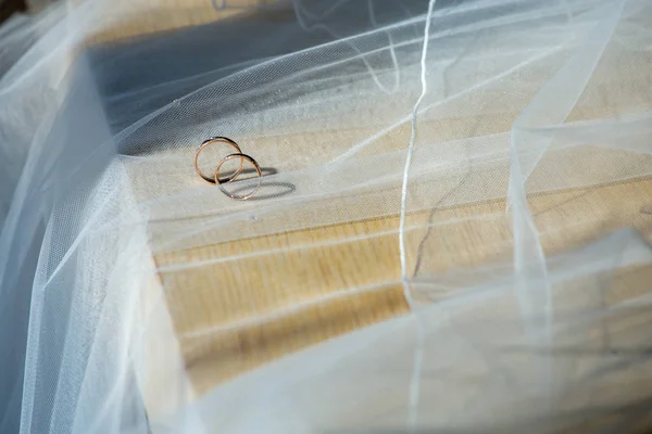 Two wedding rings on wedding veil. Gold wedding rings on the background of the white bridal veil. Rings on bridal wedding dress.