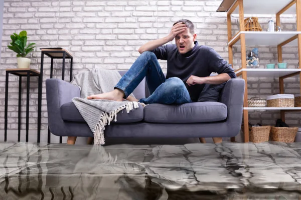 Upset Young Man Sitting Sofa Living Room Flooded Water — Stock Photo, Image