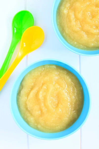Fresh homemade apple sauce in bowls with colorful spoons, photographed overhead with natural light (Selective Focus, Focus on the apple sauce in the bowls)