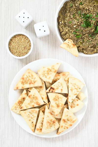 Homemade sesame pita chips with roasted eggplant dip or spread, baba ganoush in the Mediterranean cuisine on the side, photographed overhead with natural light
