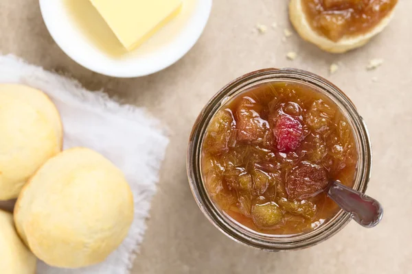 Homemade rhubarb jam in jar with scones and butter on the side, photographed overhead (Selective Focus, Focus on the jam)