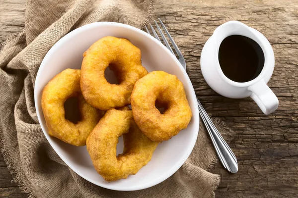 Traditional Chilean Picarones fried pastries made of pumpkin and flour yeast dough, served with sweet chancaca cane sugar sauce, photographed overhead (Selective Focus, Focus on the top of the picarones)